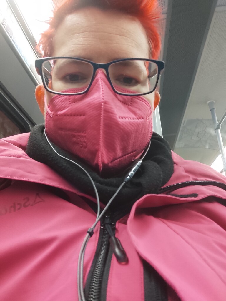 Selfie einer rothaarigen Frau mit pinker Maske und pinker Regenjacke in der U-Bahn 
