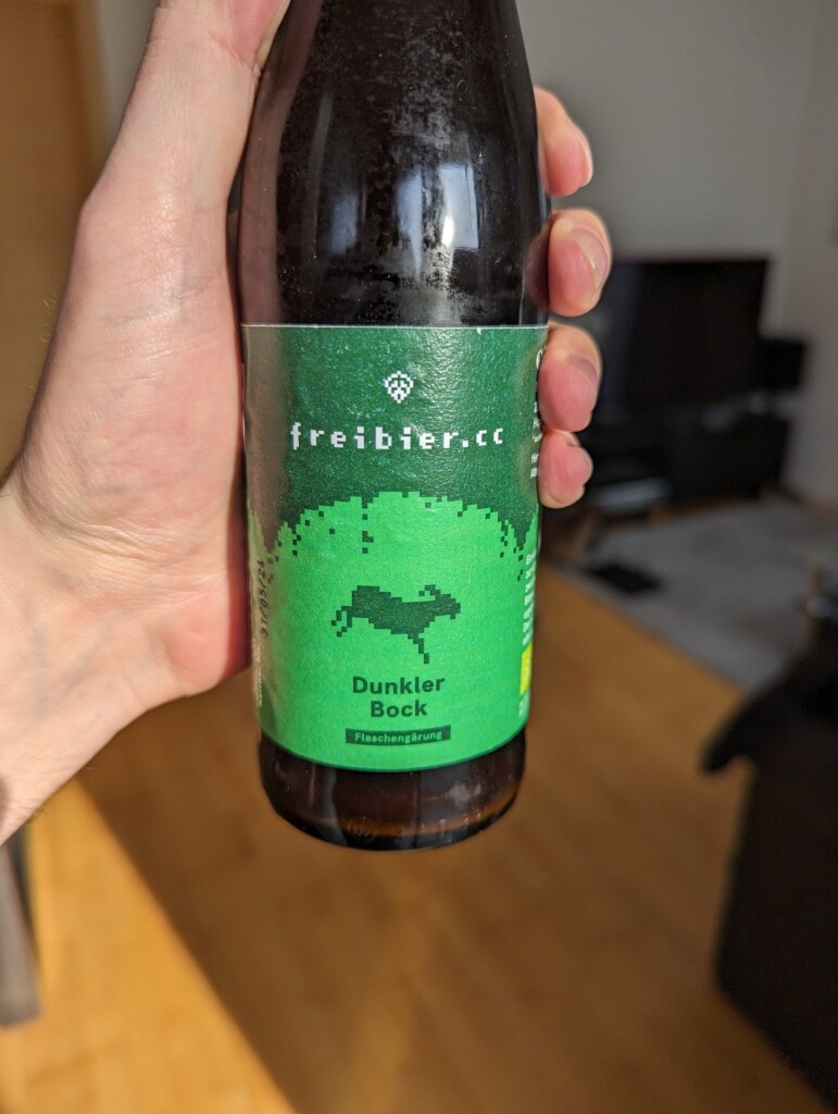 Eine Bierflasche 0,33l mit grünem Etikett in Toms Hand.