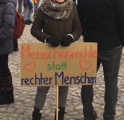 Mensch mit einem Plakat auf dem folgendes steht: „Menschenrechte statt rechter Menschen“