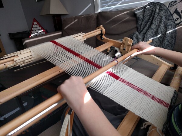 A boy weaving a scarf on a rigid heddle loom.